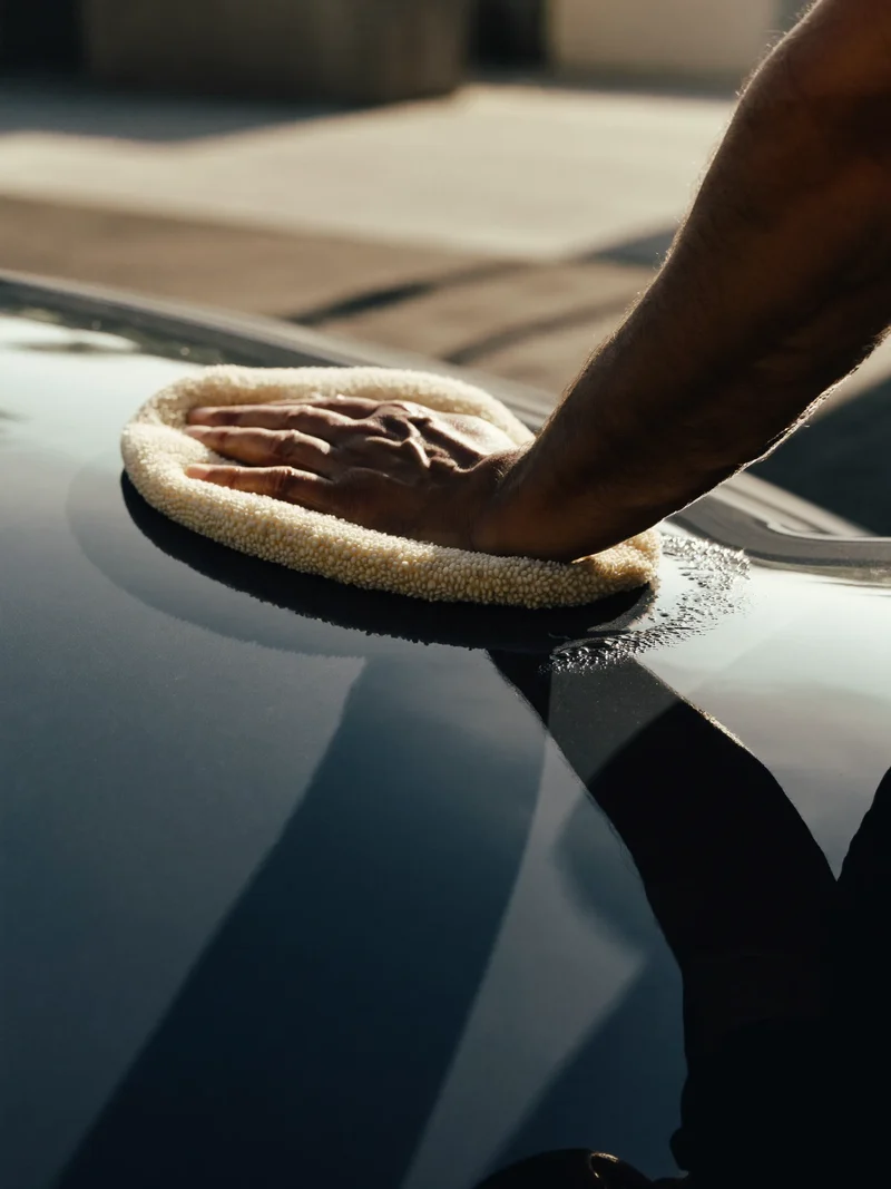 Hände polieren mit einem Mikrofasertuch die Motorhaube, Wassertropfen perlen auf dem Lack